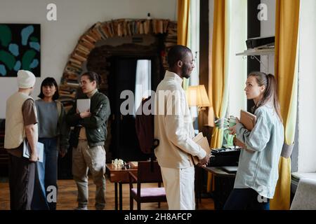 Group of students with books talking to each other while standing in the library after lessons Stock Photo