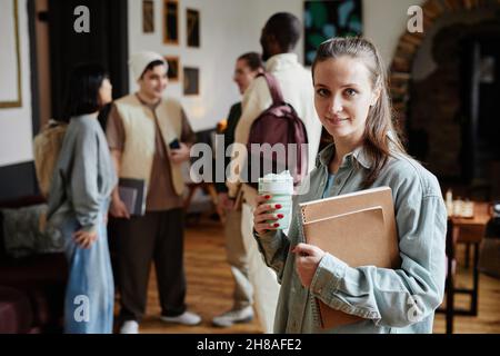 Portrait of young woman holding textbooks and coffee drink smiling at camera while studying in the university Stock Photo