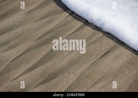 Geometric patterns in the sand and the foamy moving waves that caused them Stock Photo