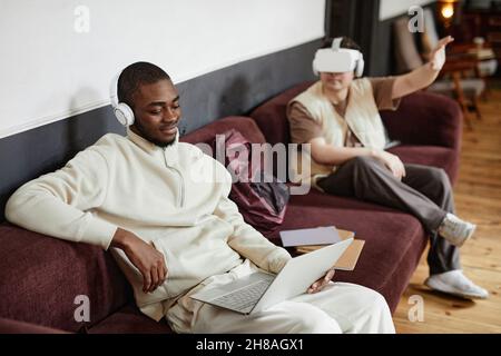 African young man in headphones watching something on laptop while resting on the sofa Stock Photo