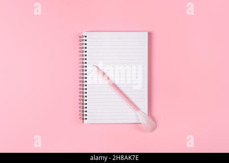 Notepad and pink pen decorated with feather on pink background. Woman power concept Stock Photo