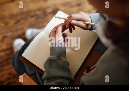 Close-up of woman sitting with notebook on her knees and writing her plans in it or doing homework Stock Photo