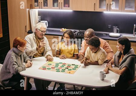 Large happy multiracial family of three generations playing board game while sitting by table in the kitchen Stock Photo
