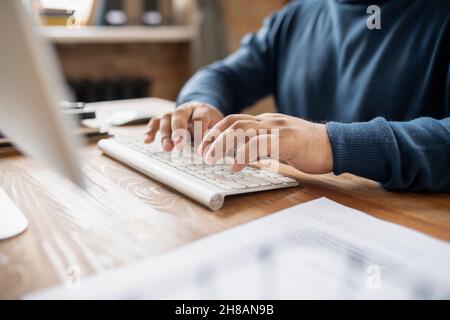 Contemporary businessman or teacher pressing buttons of keypad while sitting by table in front of computer and working Stock Photo