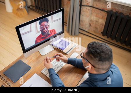 Happy young African female looking at her teacher from computer screen during discussion of subject of online lesson Stock Photo