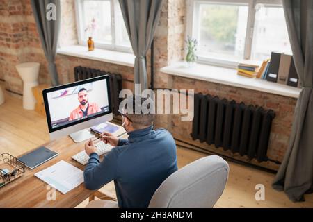 Mature man sitting in front of computer monitor and communicating to his teacher on screen during online lesson Stock Photo