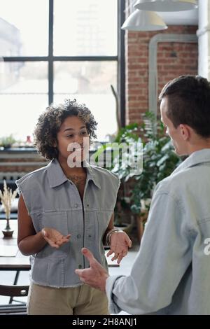 Happy young biracial businesswoman interacting with male colleague at working meeting in openspace office Stock Photo