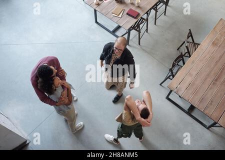 Overview of happy co-workers enjoying break while two of them embracing, man with leg prosthesis exercising and young female looking at him Stock Photo