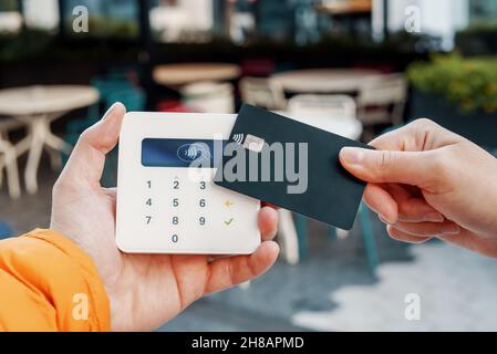 Crop faceless female client making NFC payment with plastic card on POS terminal in street cafe in city Stock Photo
