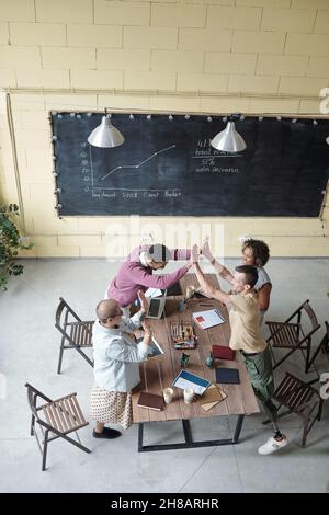 Two young successful intercultural businessmen touching by palms over workplace among female colleagues Stock Photo