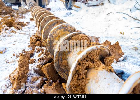 a drill auger is lying on the snow in the clay after deep exploration of the frozen soil, selective focus Stock Photo