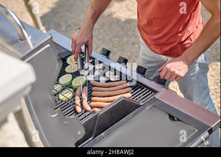 A man in red shirt standing near the barbecue grill and cooking veggies Stock Photo