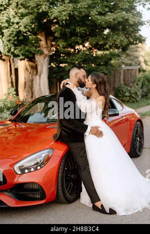 Brie and groom kissing at red car Stock Photo