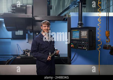 Apprentice holding a u-bolt strap in front of CNC machine Stock Photo