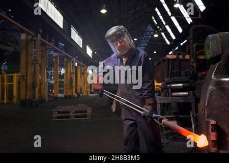 Forge worker with an upset forging of railway part Stock Photo