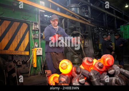 A clipped crank shaft is swung out in a pair of tongs from the clipping press into a steel container Stock Photo