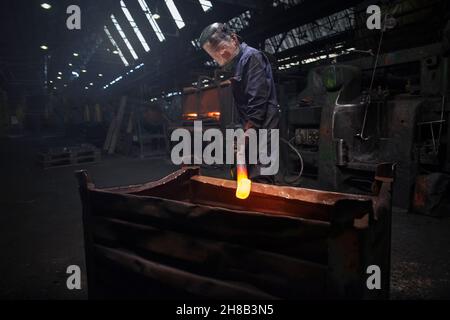 Forge worker preparing to release finished upset forging into steel container Stock Photo
