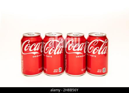 A line of four cans of Coca Cola, original taste, also known as Coke Classic, in traditional red and white cans. Stock Photo