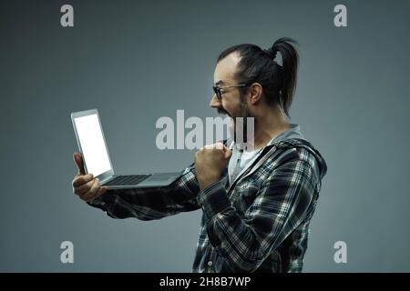Exuberant ecstatic man exclaiming - OMG I've won! - as he pumps the air with his fist while looking at the screen of a handheld laptop balanced on his Stock Photo