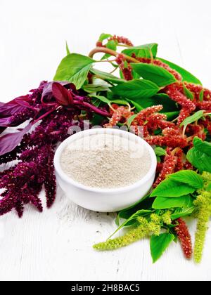 Amaranth flour in a bowl, brown, green and purple flowers of a plant on wooden board background Stock Photo