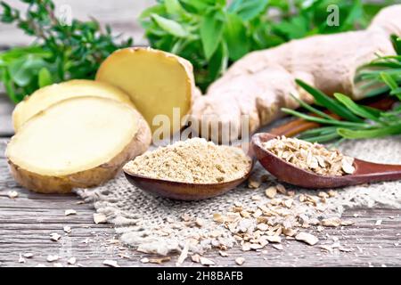 Ground ginger and flakes in two wooden spoons, ginger root on burlap, spicy herbs on a wooden board background Stock Photo