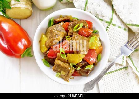 Beef with oranges, bell peppers and ginger root in bowl, a napkin and a fork on wooden board background from above Stock Photo