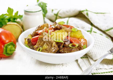 Beef with oranges, bell pepper and ginger root in a bowl, towel and a fork on wooden board background Stock Photo