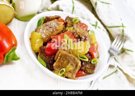 Beef with oranges, bell pepper and ginger root in bowl, a napkin and a fork on the background of light wooden board Stock Photo
