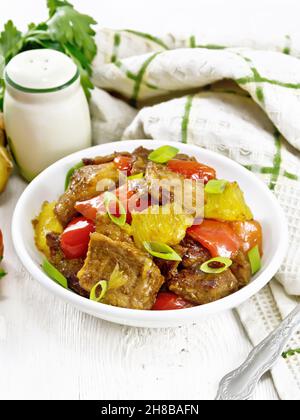 Beef with oranges, bell peppers and ginger root in bowl, a napkin and a fork on wooden board background Stock Photo