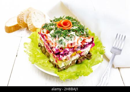 Puff salad with beef, boiled potatoes and beets, pears, spicy Korean carrots, seasoned with mayonnaise and garnished with dill on a green lettuce in a Stock Photo