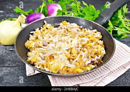 Fried turnips with onions in a frying pan on towel on wooden board background Stock Photo