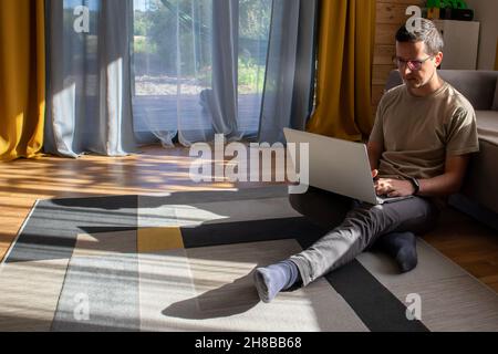 A guy in casual clothes is working on the floor in a sunny loft apartment Stock Photo