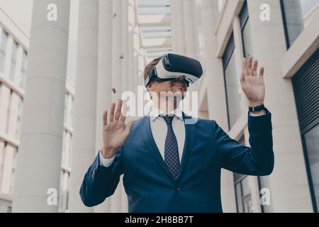 Man in formal blue suit walking around in virtual reality while wearing VR goggles Stock Photo