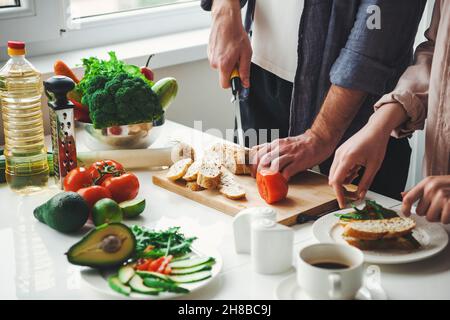 Angle view of couple's hands preparing the meal, chopping bread for sandwiches in their kitchen. Vegetarian healthy food. Healthy vegetarian lunch Stock Photo