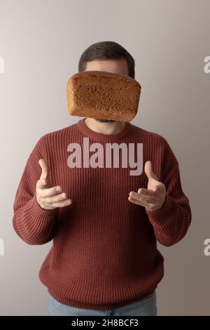 A man in a sweater throw up a loaf of rye bread into the air. Front view. Portrait. Stock Photo