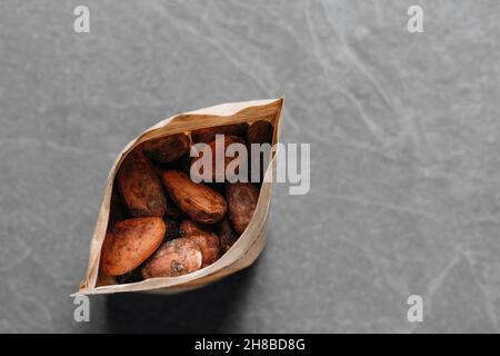 Cacao beans on grey concrete background packed in bag. Raw fermented, organic cocoa seeds for hot chocolate drink. Flat lay, copy space for food Stock Photo