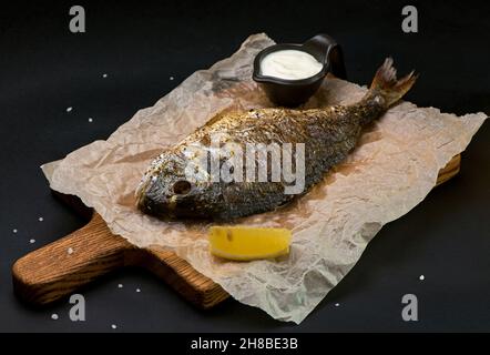 delicious roasted dorado or sea bream fish with lemon slices, spices, fresh rosemary on dark wooden table view from above Stock Photo