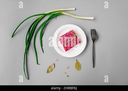 Russian herring salad under a fur coat on gray background. Green onion around plate, top view. Stock Photo