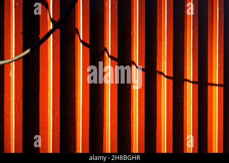 wooden slats on houses painted in orange with shadows from cords Stock Photo