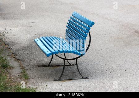 Freshly painted blue wooden boards on top of vintage retro black metal frame public bench mounted on paved sidewalk next to uncut grass Stock Photo