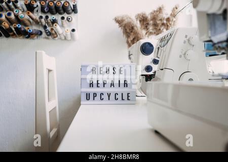 Reuse, repair, upcycle text on light board on sewing machines background. Stack of old jeans, Denim clothes, scissors, thread and sewing tools in Stock Photo