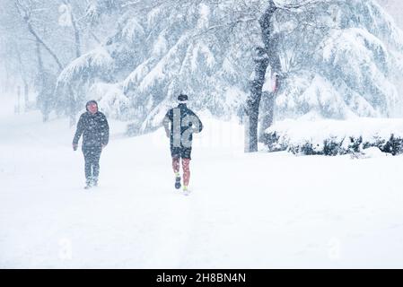 Madrid, Spain - January 9, 2021: Man runningg on a city street covered in snow during heavy snowfall with fallen trees. Storm Filomena in Madrid. Artu Stock Photo