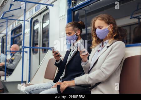 passengers wearing protective masks using their smartphones while sitting in a subway car. Stock Photo