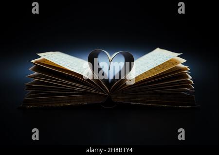 Music is the literature of the heart. Opened antiquarian book with sheet music and pages curved into a heart shape. Stock Photo