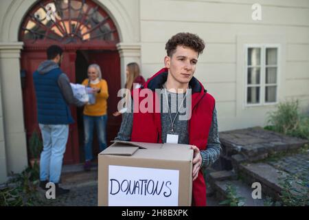 Group of young volunteers giving donation box to senior woman standing in door, social care concept Stock Photo