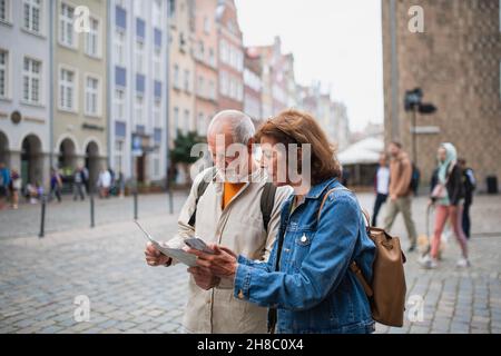 Portrait of senior couple tourists using map and smartphone outdoors in town street Stock Photo