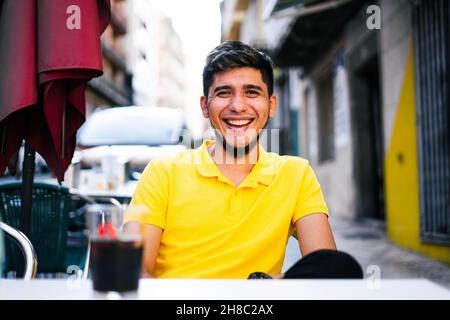 Closeup of the young man sitting on a terrace looking at the camera smiling. Stock Photo