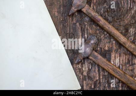 Old rusty hand tools. Two hammers and a sheet of paper on a cracked wooden surface. Top view. Selective focus. Stock Photo