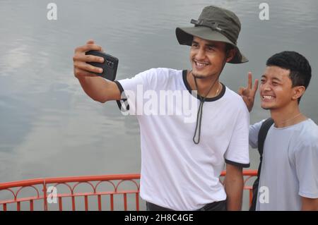 Two south asian young guys smiling with taking selfie together by the lake with copy space Stock Photo
