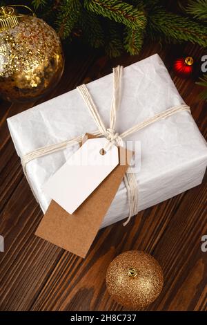 Christmas Gift Tag mockup. White minimal gift box on wooden table with festive decorations. Stock Photo